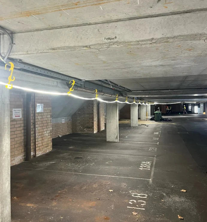 Underground parking garage with concrete walls and floor, illuminated by hanging lights.